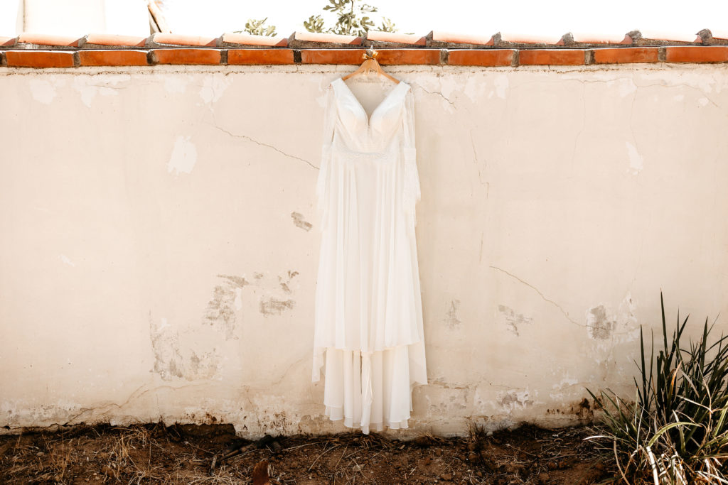 Boho wedding dress hung on a spanish style wall

