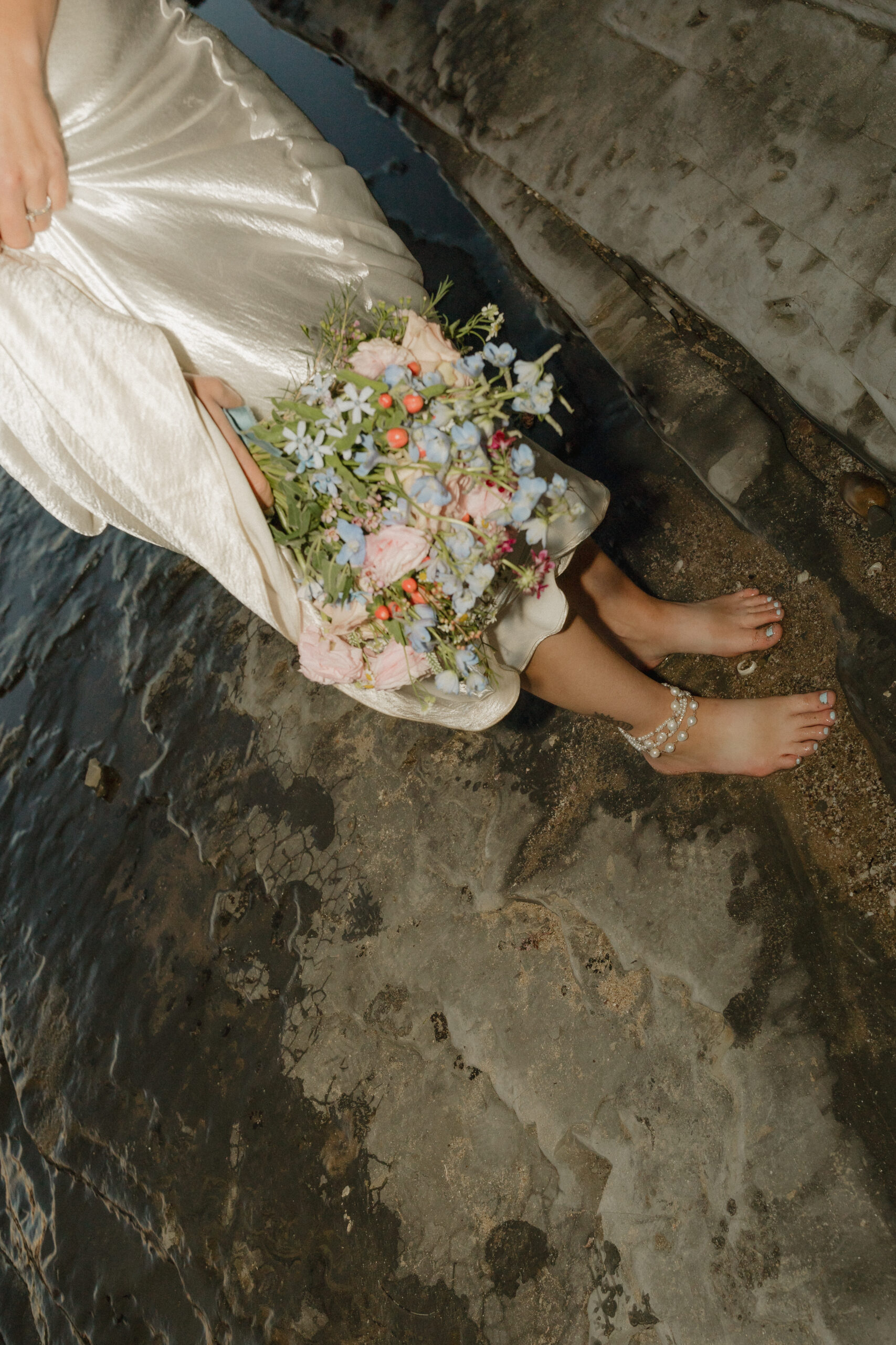 Brides feet with anklets and her flowers