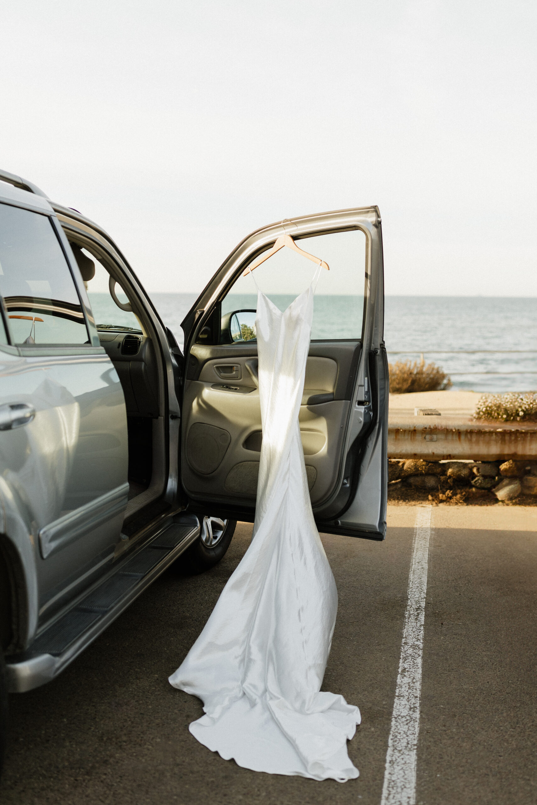 Wedding dress hangin on the car door with an ocean background