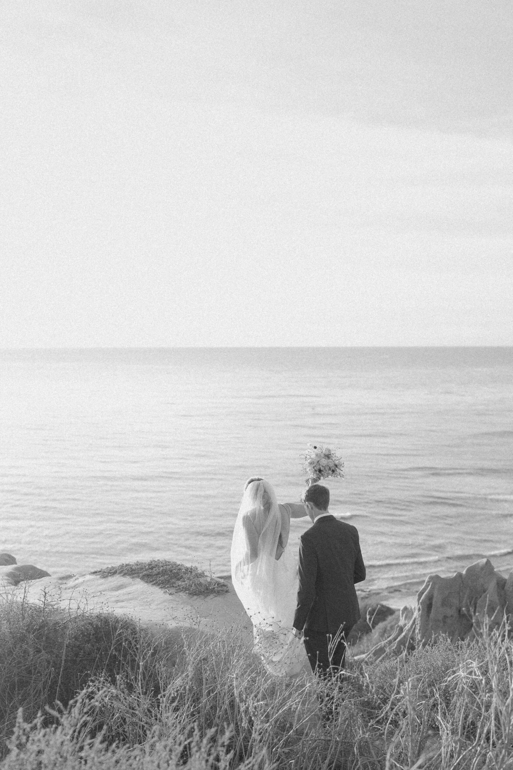 Black and white of bride and groom walking atop the cliffs