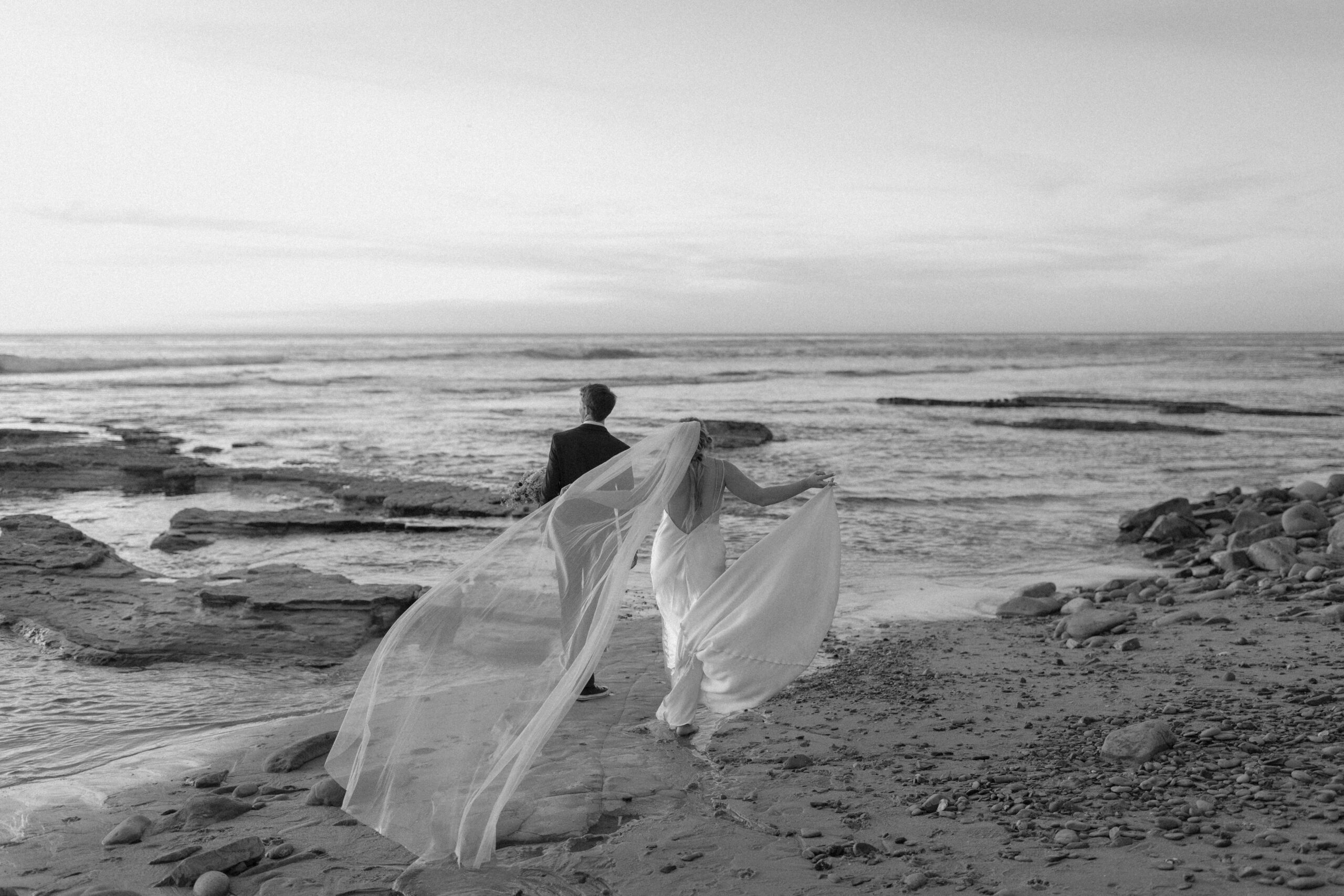 Black and white of couple walking out towards the ocean